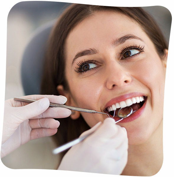 A woman smiling as a dentist examines her teeth with a dental mirror and a probe.