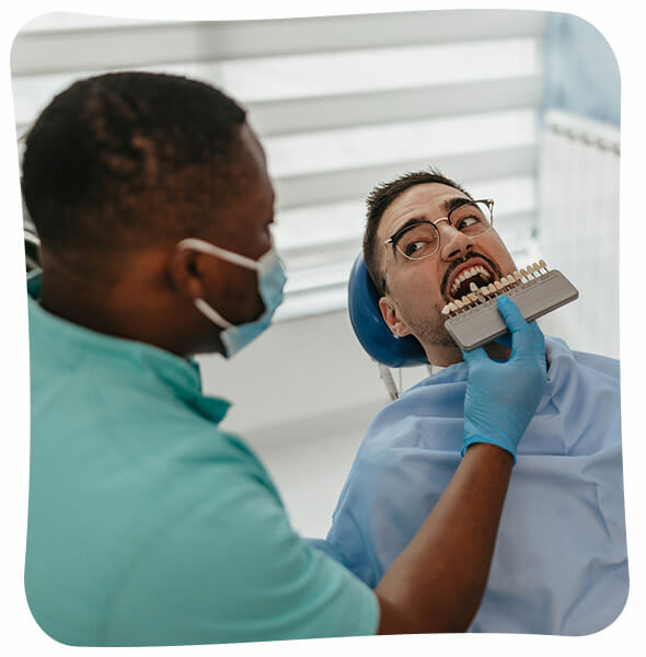 A patient undergoing a dental shade matching procedure with a dentist holding a shade guide to his teeth.