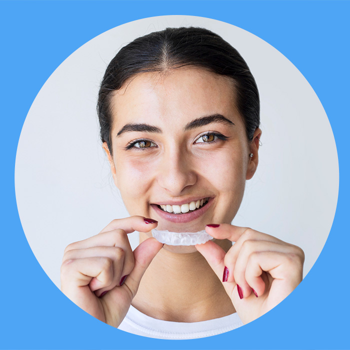 A smiling young woman holding a clear Invisalign aligner in front of her teeth.