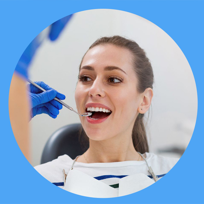 A woman in a dental chair receiving an oral examination by a dentist wearing blue gloves.